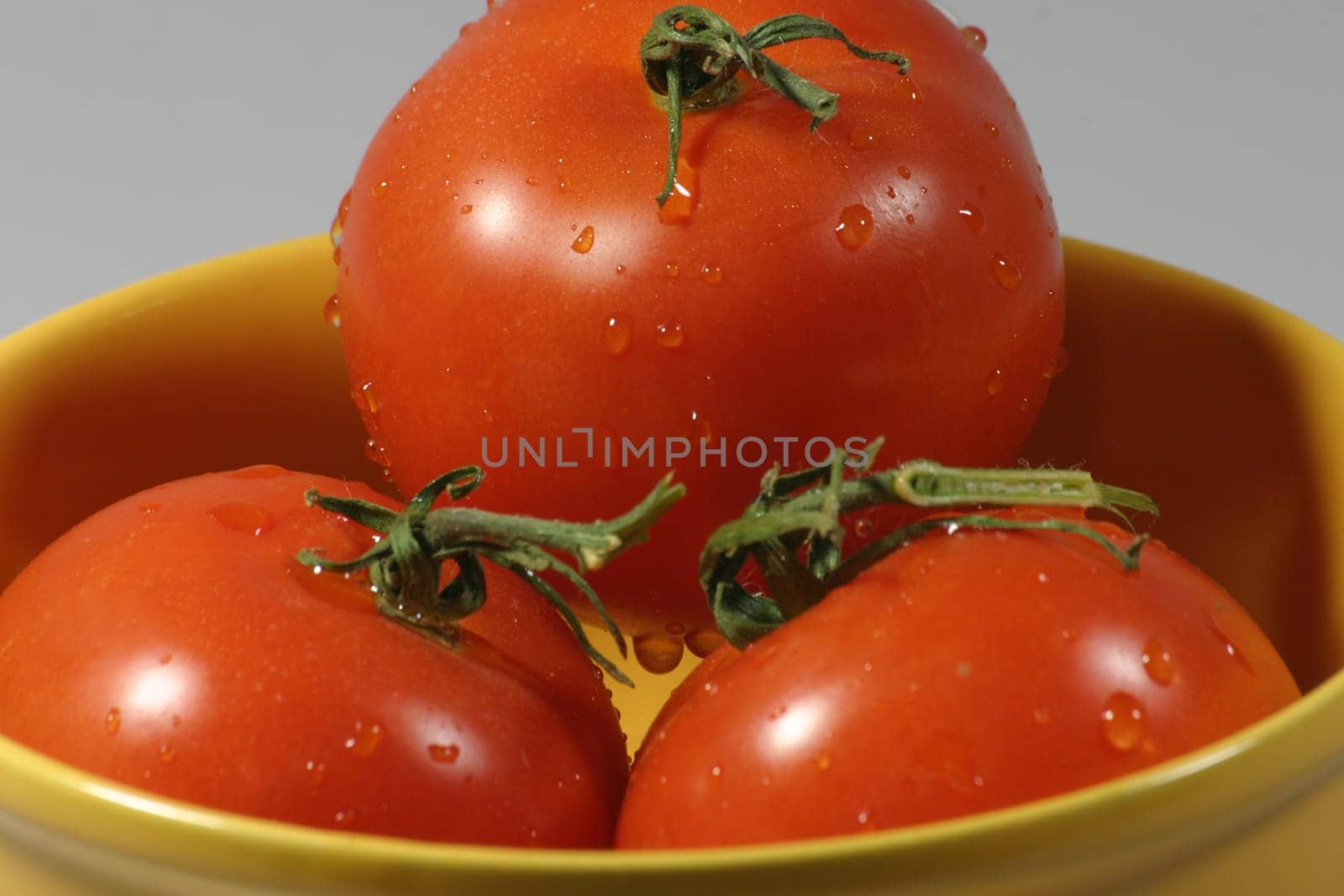 Three freshly washed tomatoes in a yellow bowl