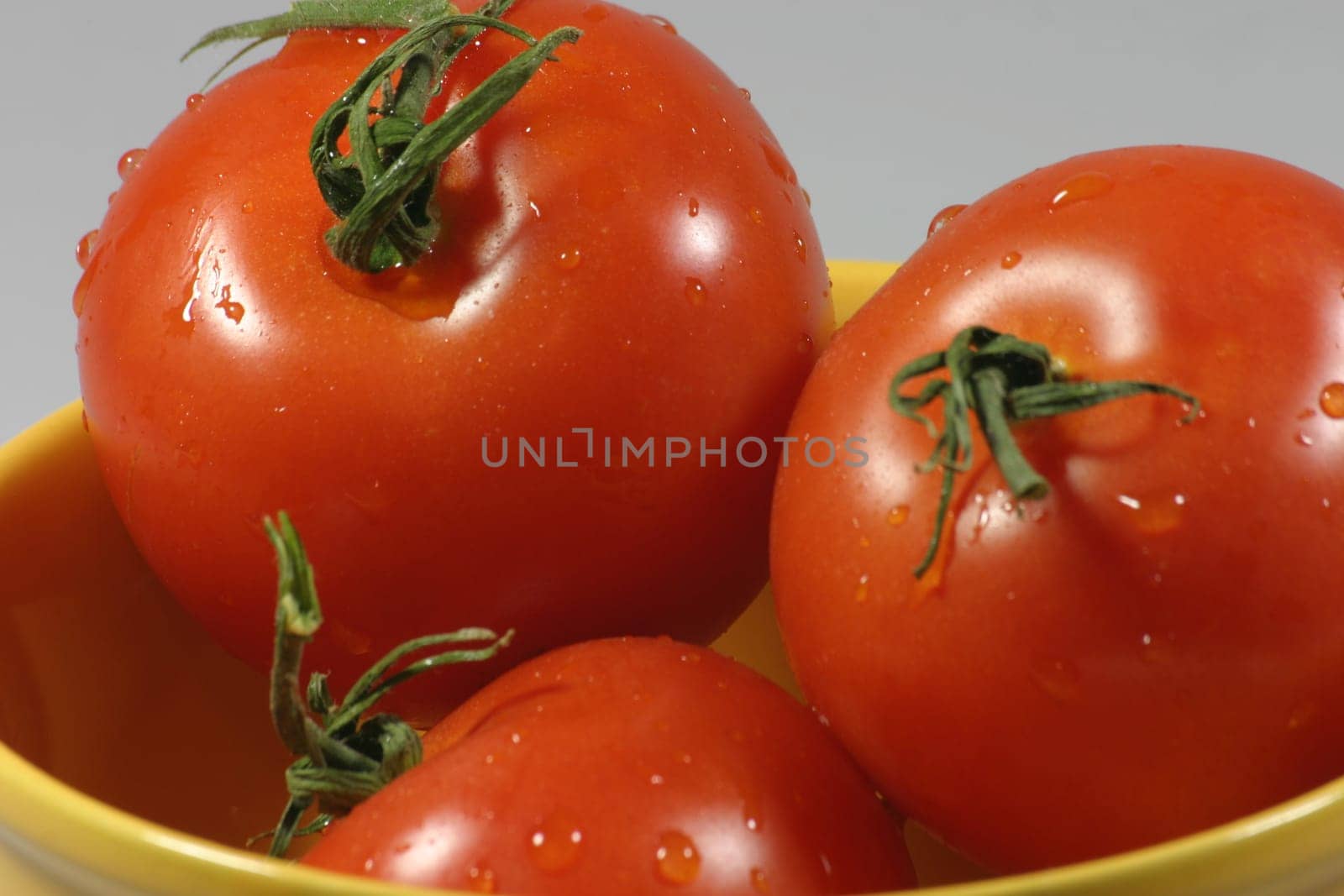 Three freshly washed tomatoes in a yellow bowl