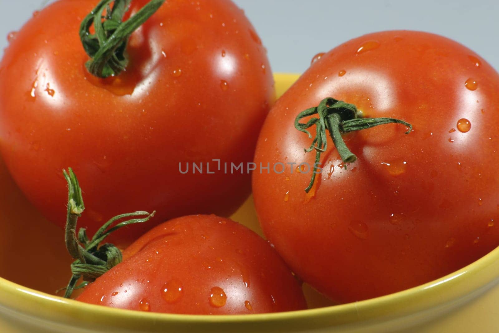 Three freshly washed tomatoes in a yellow bowl
