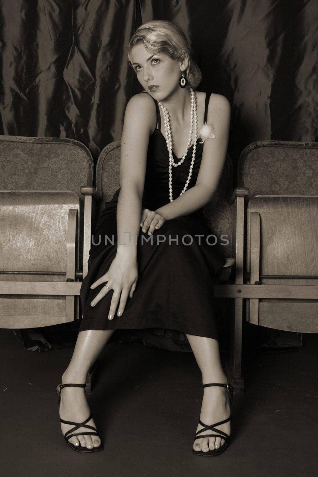 A woman dressed in the style of the 20s sits intently in the cinema with her hands on her knees