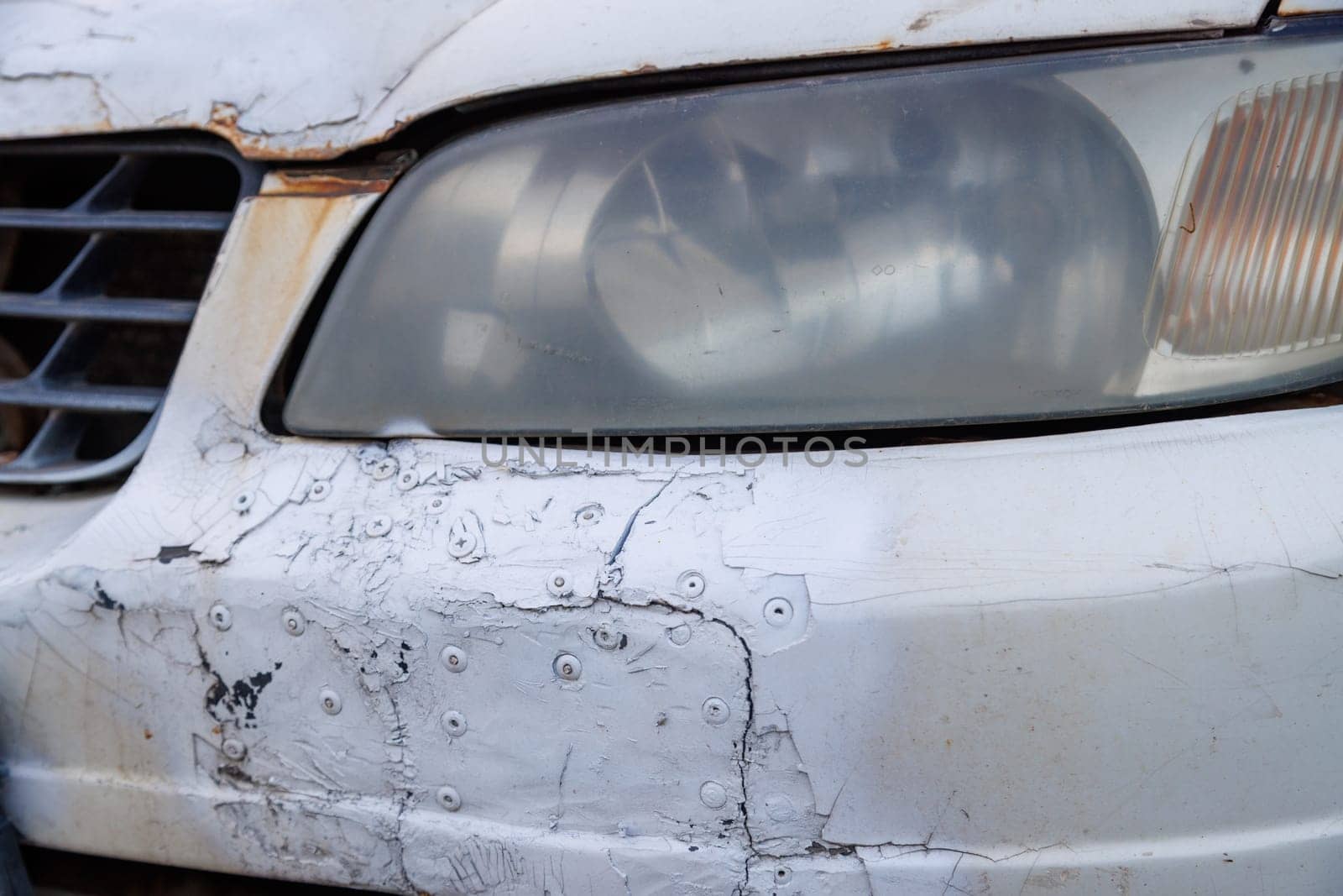 old white car bumper neglectly fixed with patches and rivetts and painted over with can of spraypaint, closeup view by z1b