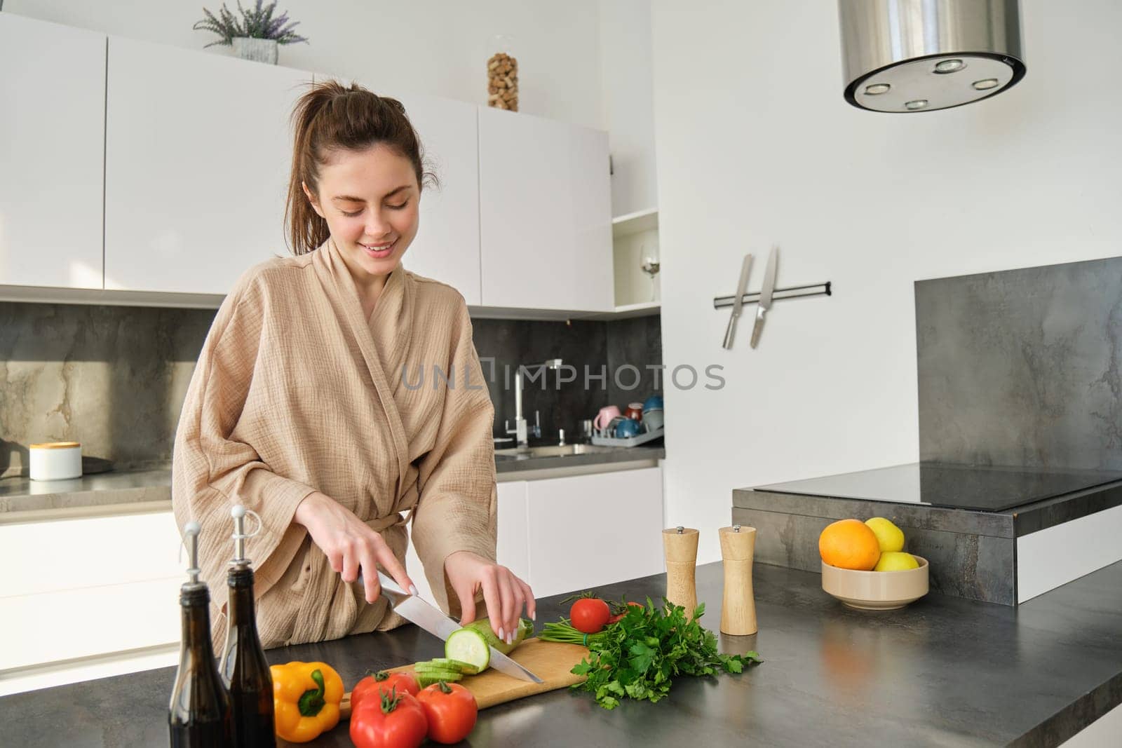 Portrait of good-looking woman cooking salad in the kitchen, chopping vegetables and smiling, preparing healthy meal, leading healthy lifestyle and eating raw food by Benzoix