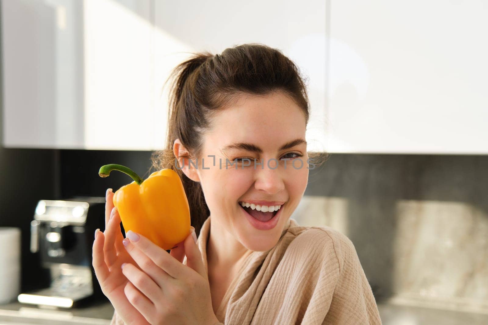 Close up portrait of cute winking girl, showing yellow pepper, standing in kitchen, making vegetarian meal, making salad, eating healthy vegetables by Benzoix