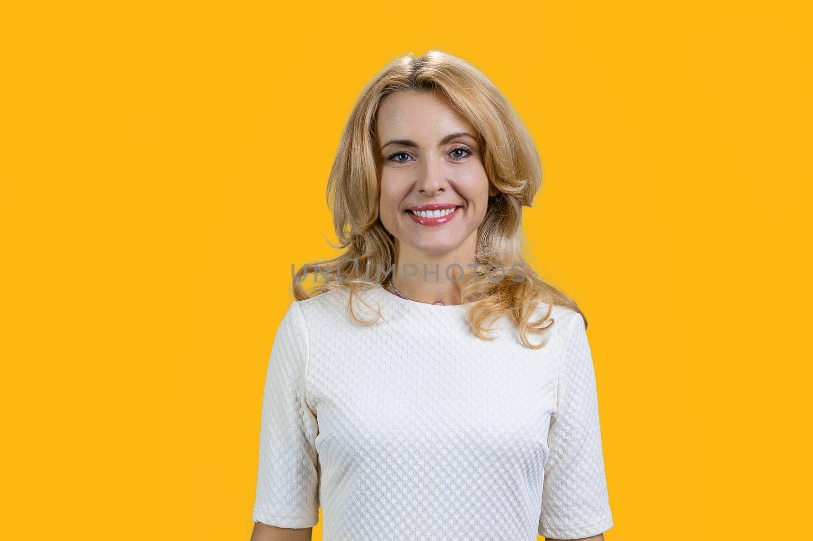 Happy mature blond woman in a white blouse. Isolated on orange.