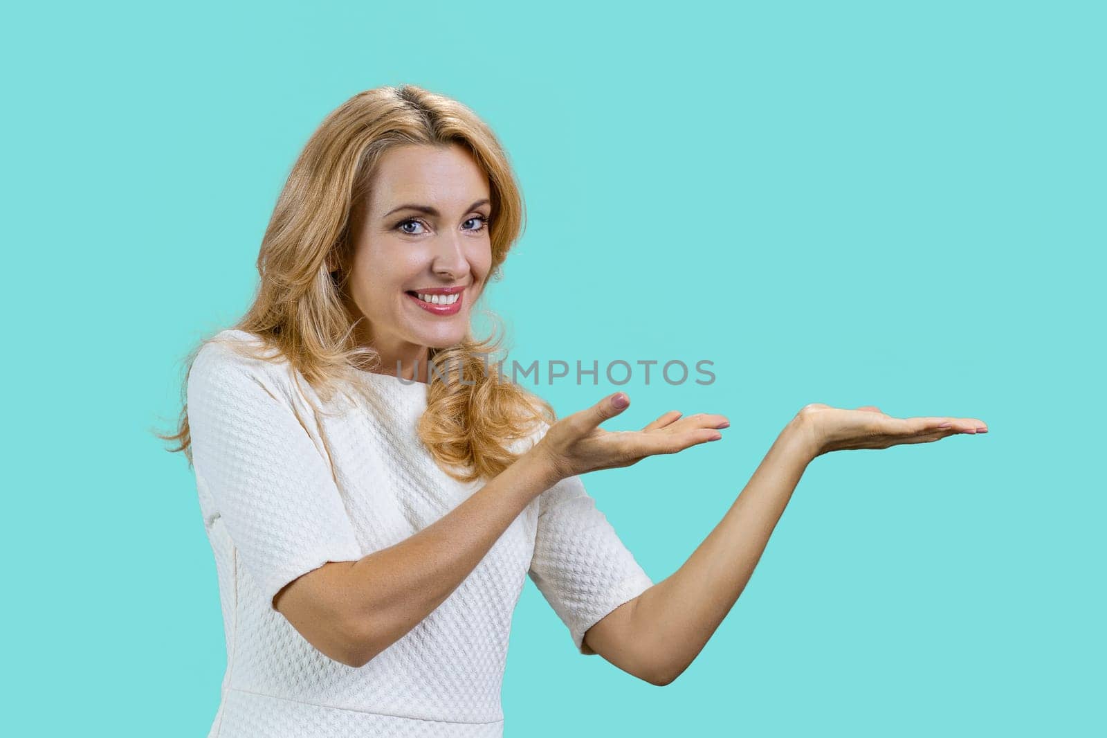 Portrait of a mature caucasian woman presenting copy space with both hands. Isolated on turquoise.