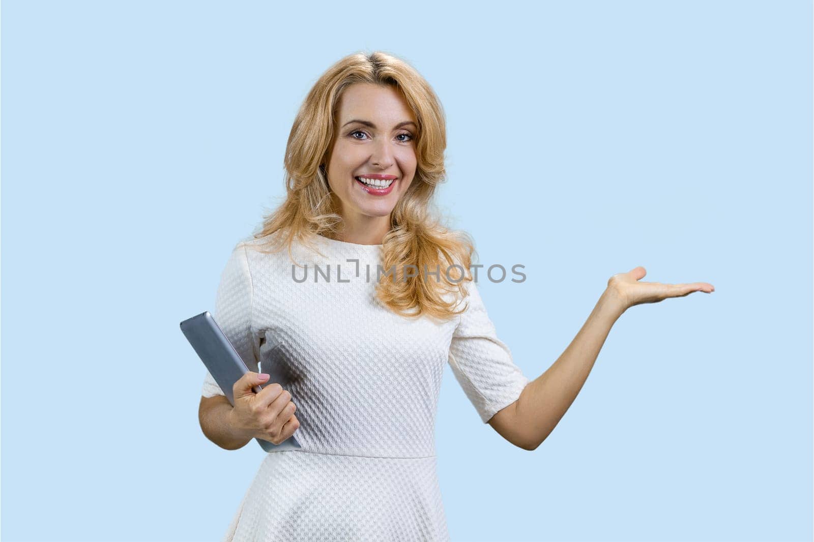 Portrait of a mature happy caucasian woman holding a tablet device and showing copy space. Isolated on pale blue.