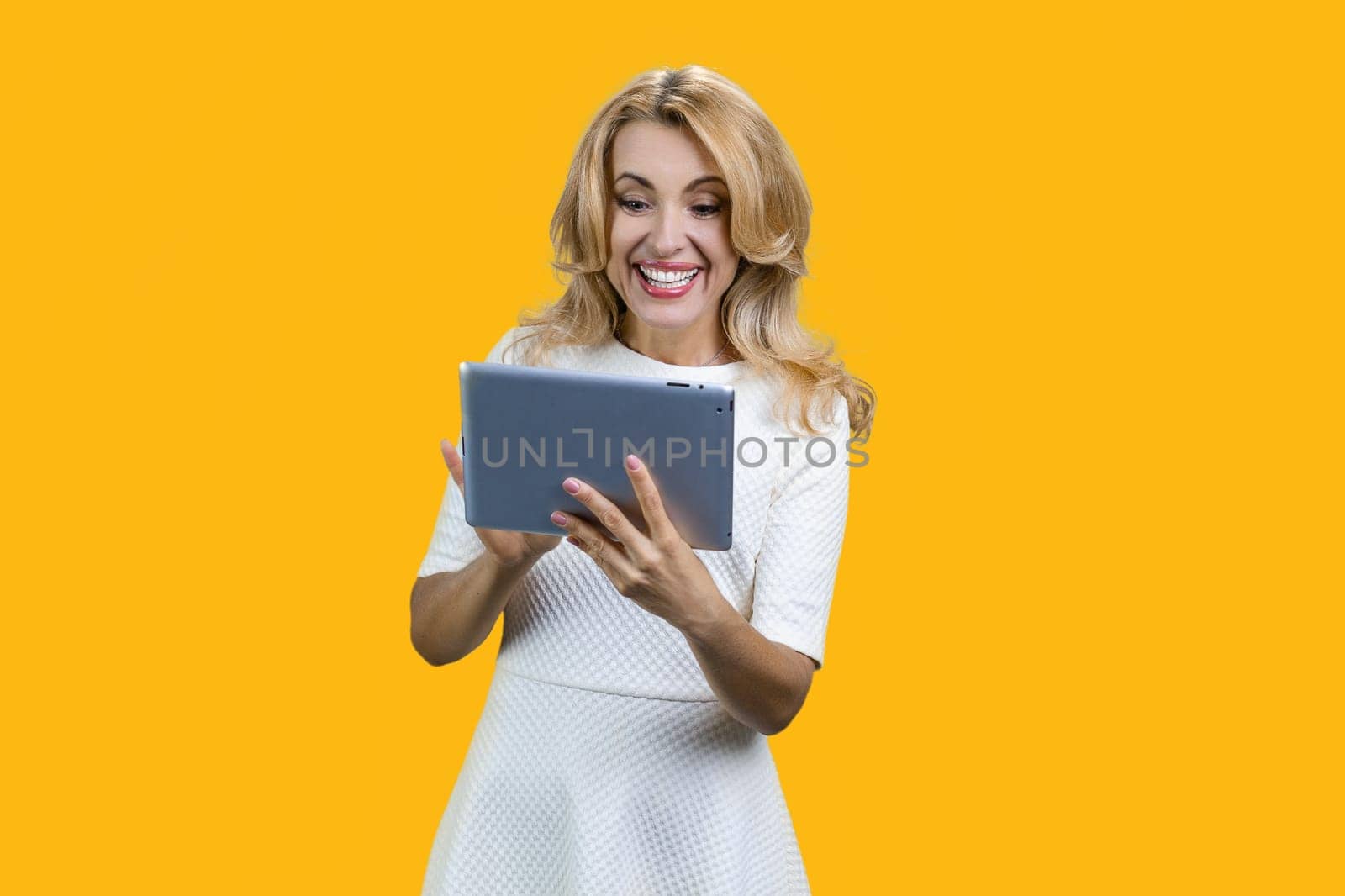 Happy middle middleaged woman using digital tablet. Isolated on yellow.