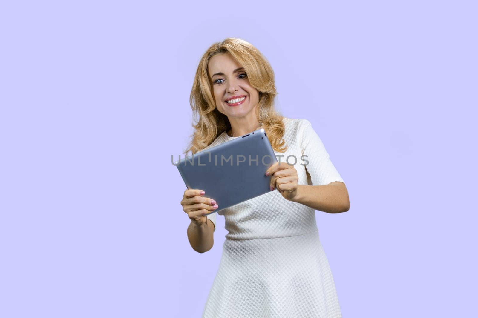 Portrait of happy mature lady plays video game on the tablet device. Isolated on purple.