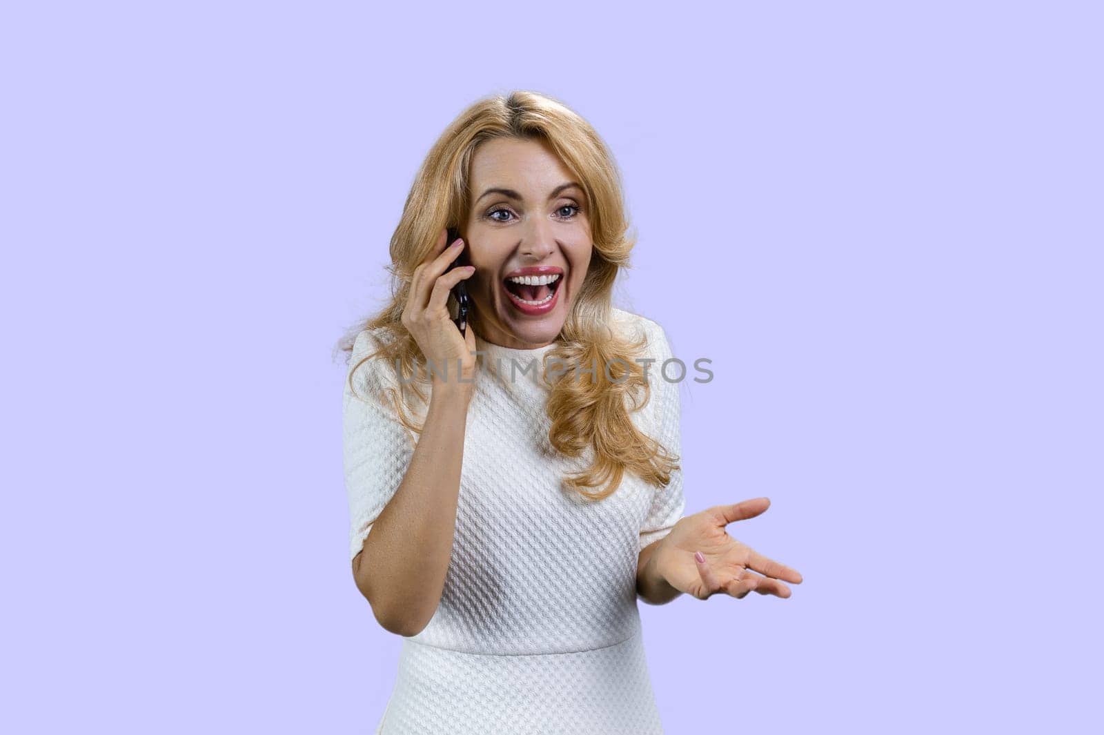 Emotional happy mature blonde woman talking on the phone. Isolated on purple.