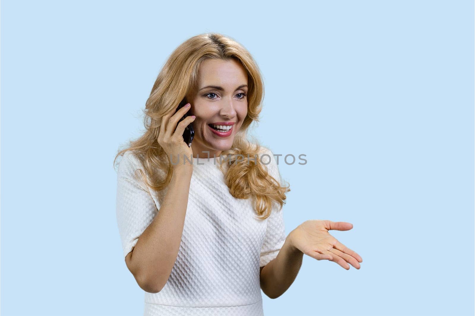 Portrait of happy mature blonde talking on the phone. Isolated pastel blue background.