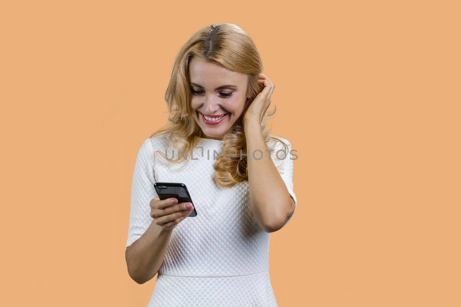 Portrait of attractive blonde mature woman using her smartphone. Isolated on beige background.