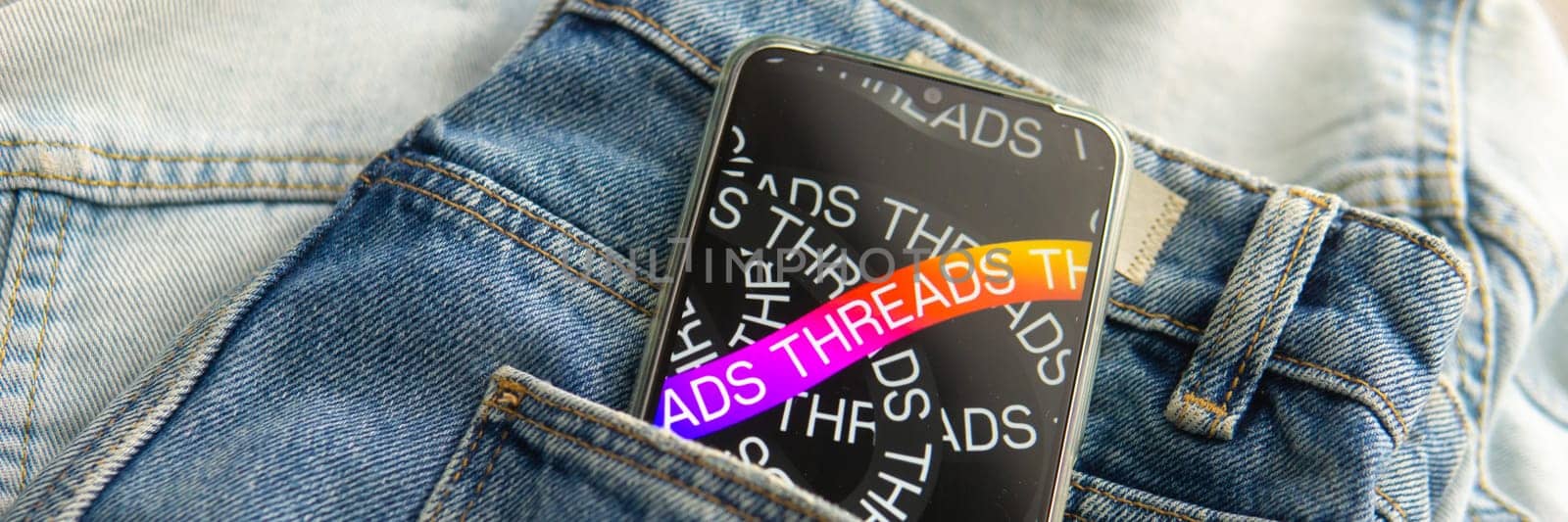 Tver, Russia - July 15, 2023, the threads logo on the smartphone screen lying on the jeans. The threads icon. The logo of the current application. Threads social network