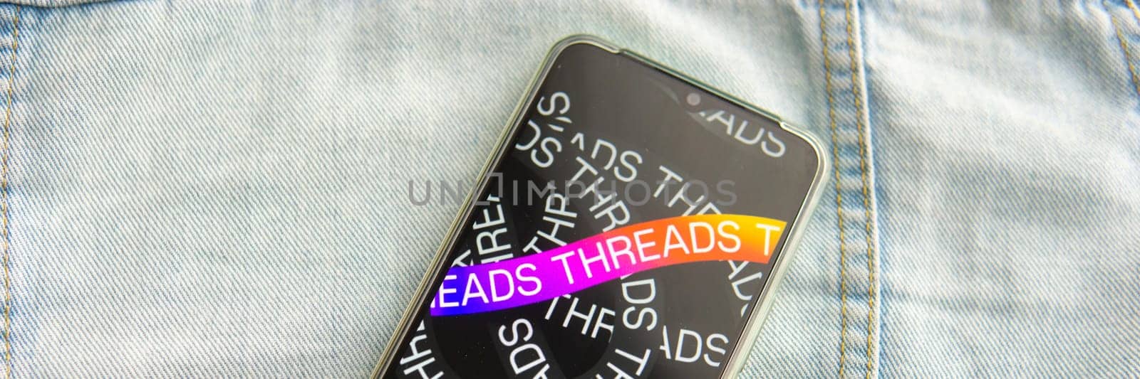 Tver, Russia - July 15, 2023, the threads logo on the smartphone screen lying on the jeans. The threads icon. The logo of the current application. Threads social network