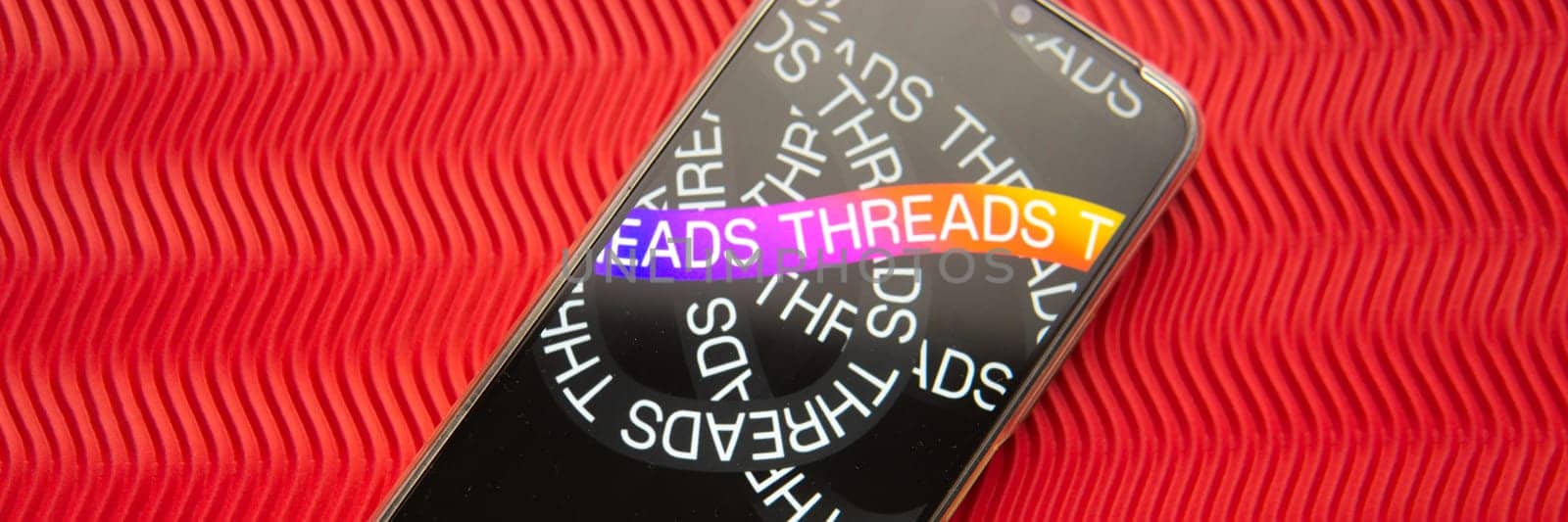 Tver, Russia - July 15, 2023, threads logo on the smartphone screen, on a red background. The threads icon. The logo of the current application. Threads social network. by Annu1tochka
