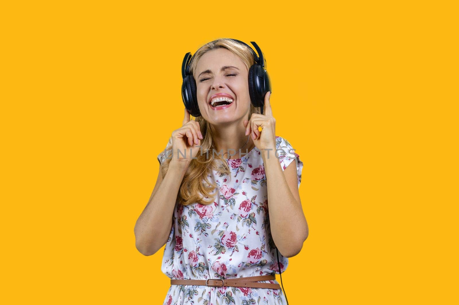 Blonde woman enjoys music in headphones. Isolated on yellow.