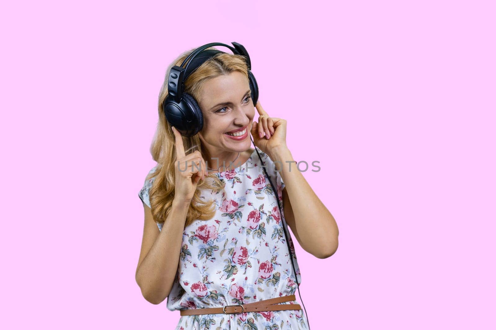 Blonde woman listening to music in headphones. Isolated on pink.