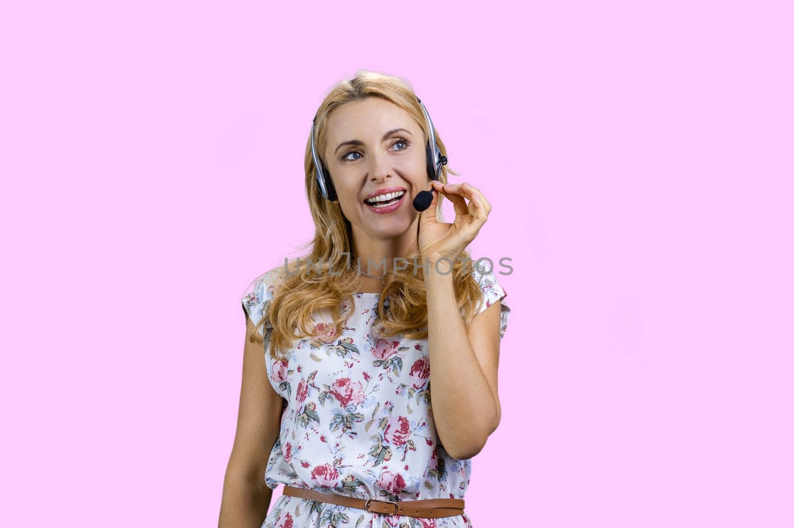 Portrait of happy cheerful blonde woman wearing headset. Isolated on pink.