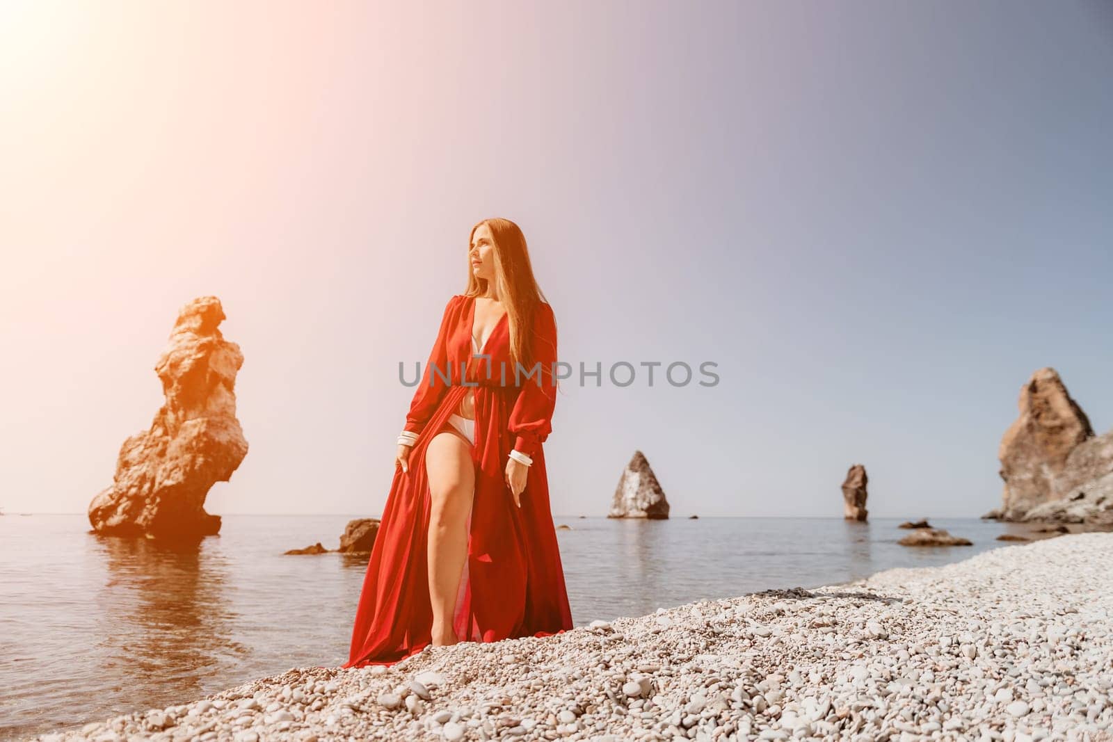 Woman travel sea. Happy tourist in red dress enjoy taking picture outdoors for memories. Woman traveler posing on the rock at sea bay surrounded by volcanic mountains, sharing travel adventure journey by panophotograph