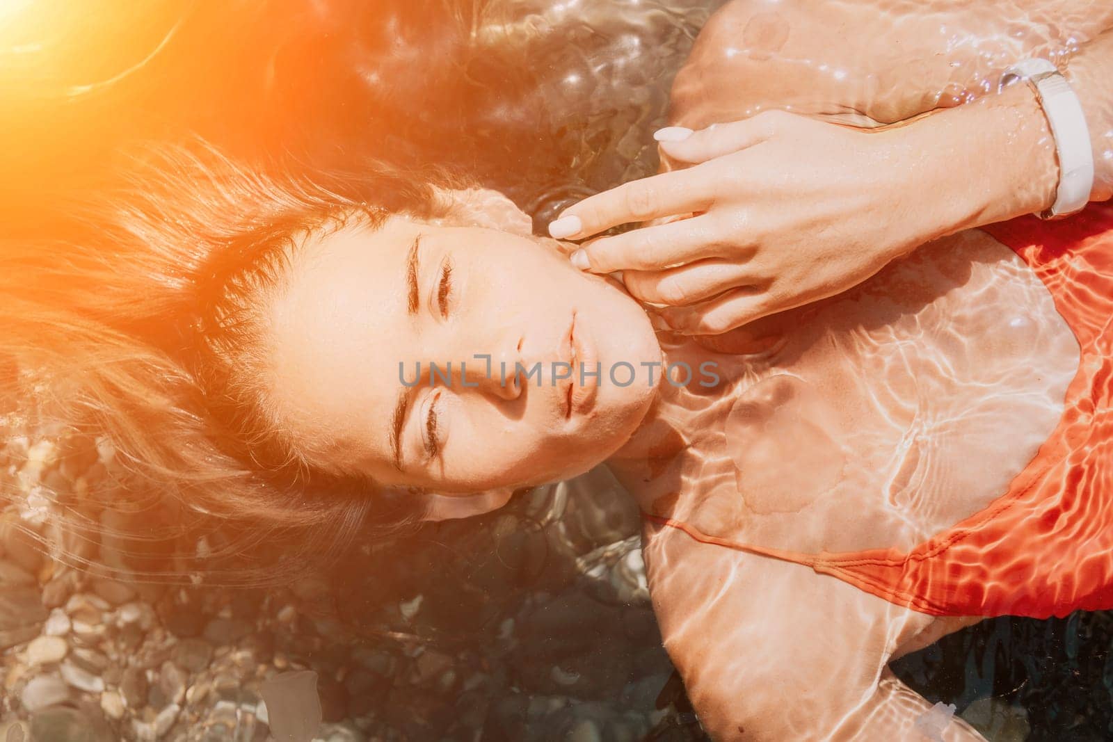 Woman travel portrait. close-up portrait of a happy woman with long hair in a red bikini, floating in water and smiling at the camera. by panophotograph