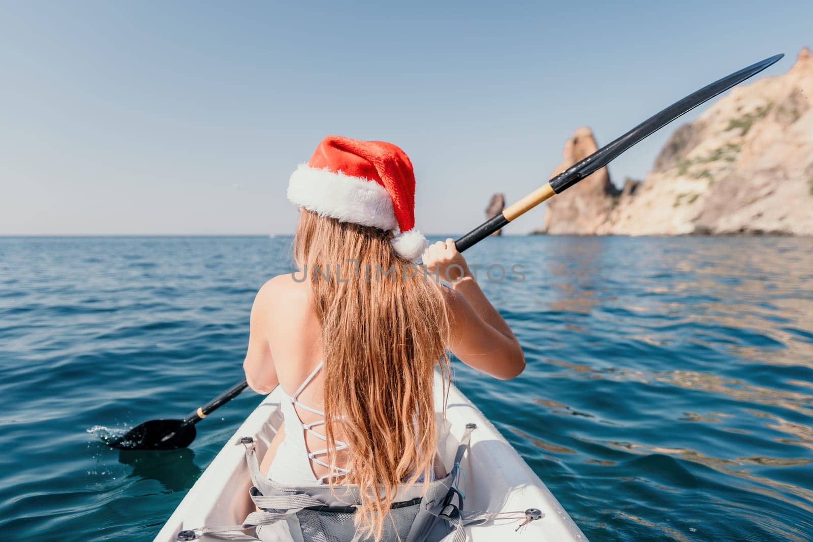 Woman in kayak back view. Happy young woman with long hair floating in transparent kayak on the crystal clear sea. Summer holiday vacation and cheerful female people relaxing having fun on the boat