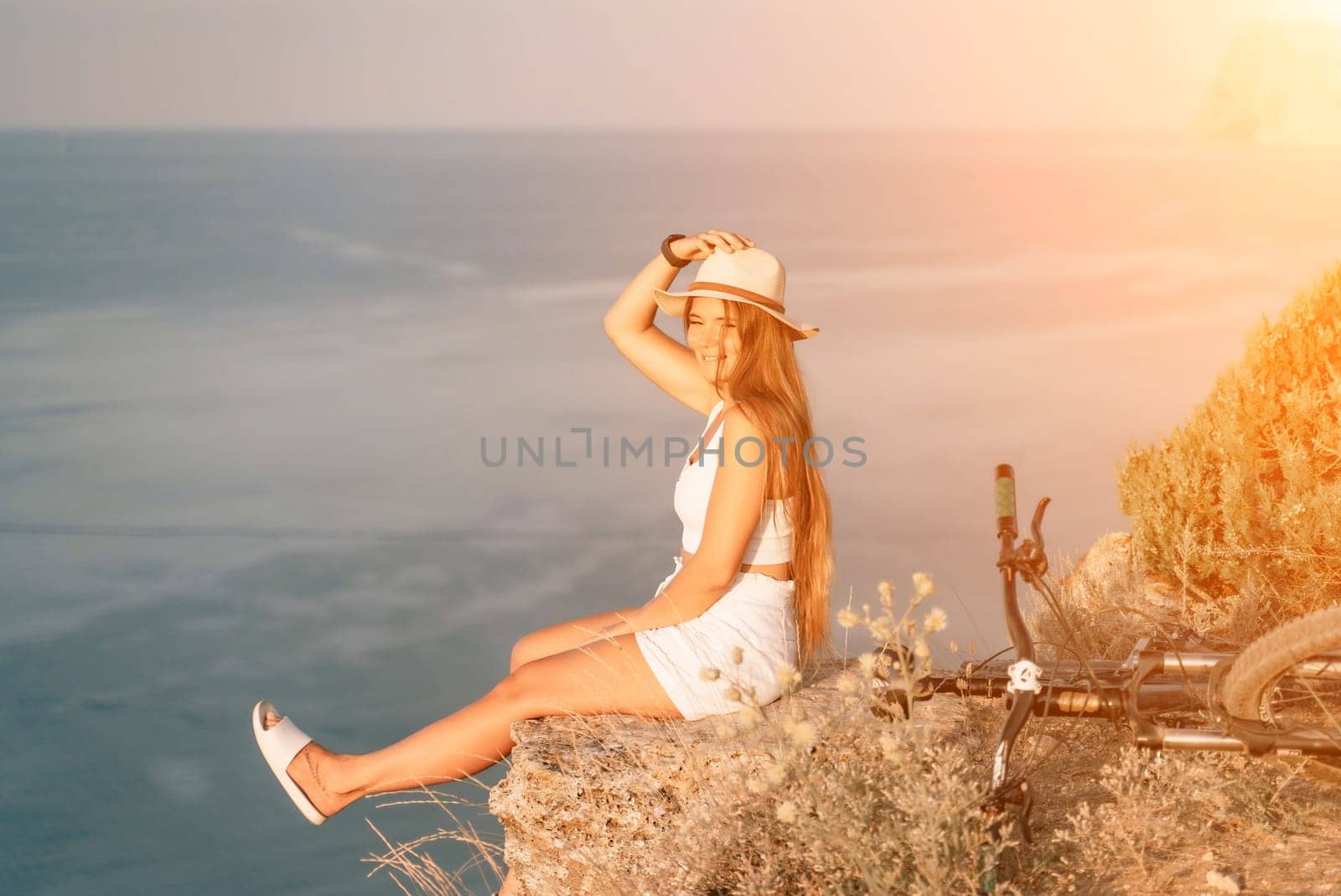 A woman cyclist on a mountain bike looking at the landscape of mountains and sea. Adventure travel on bike