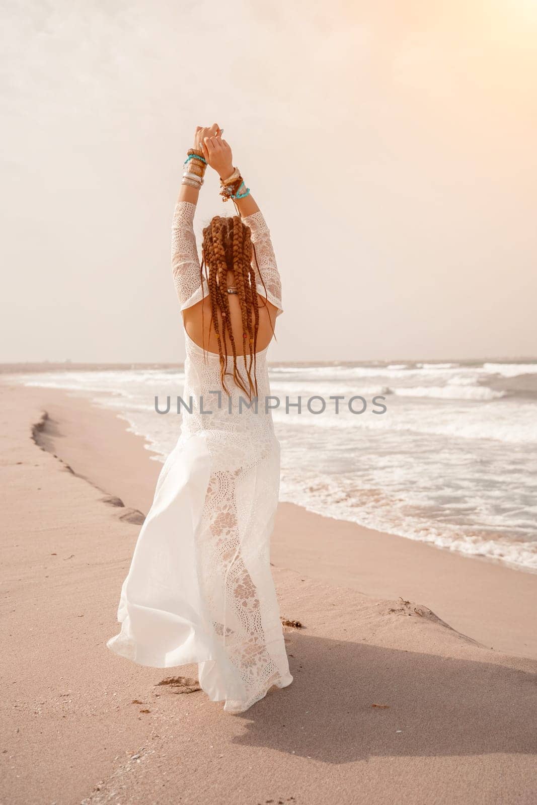 woman sea white dress. Model in boho style in a white long dress and silver jewelry on the beach. Her hair is braided, and there are many bracelets on her arms. by Matiunina