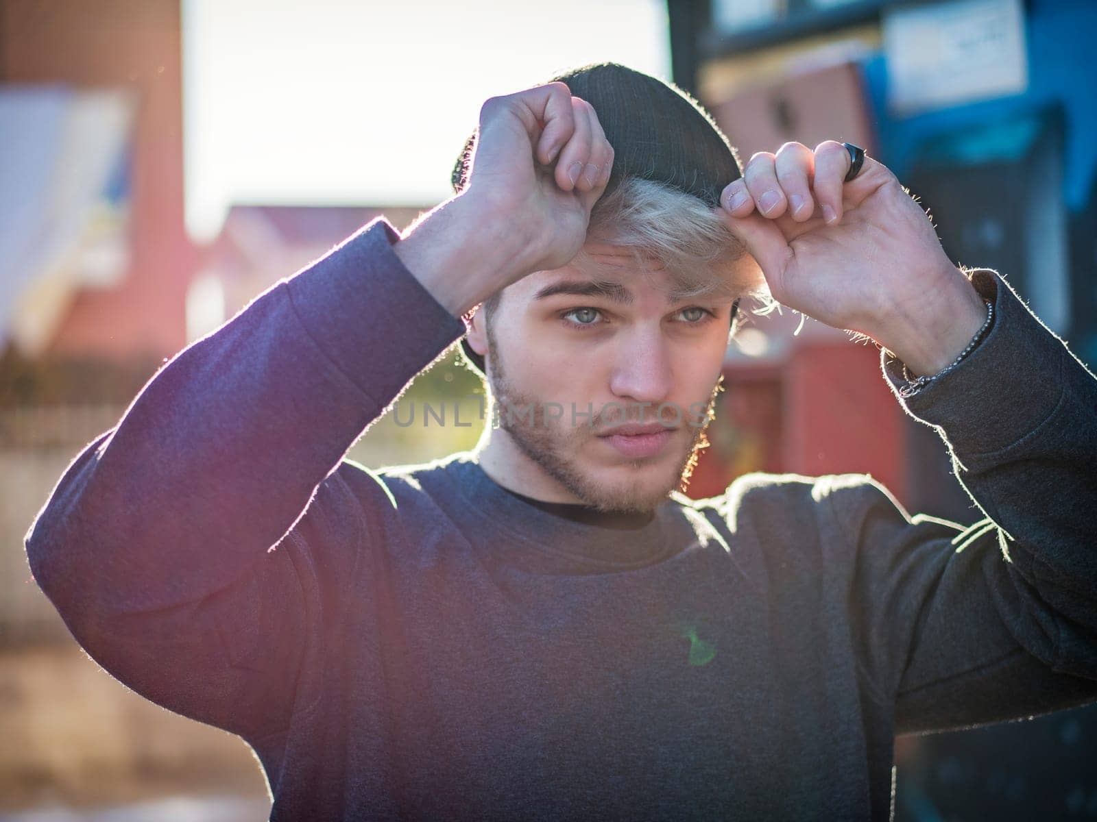 A young handsome man holding his hat over his head. Photo of a man shielding himself from the sun with his hat