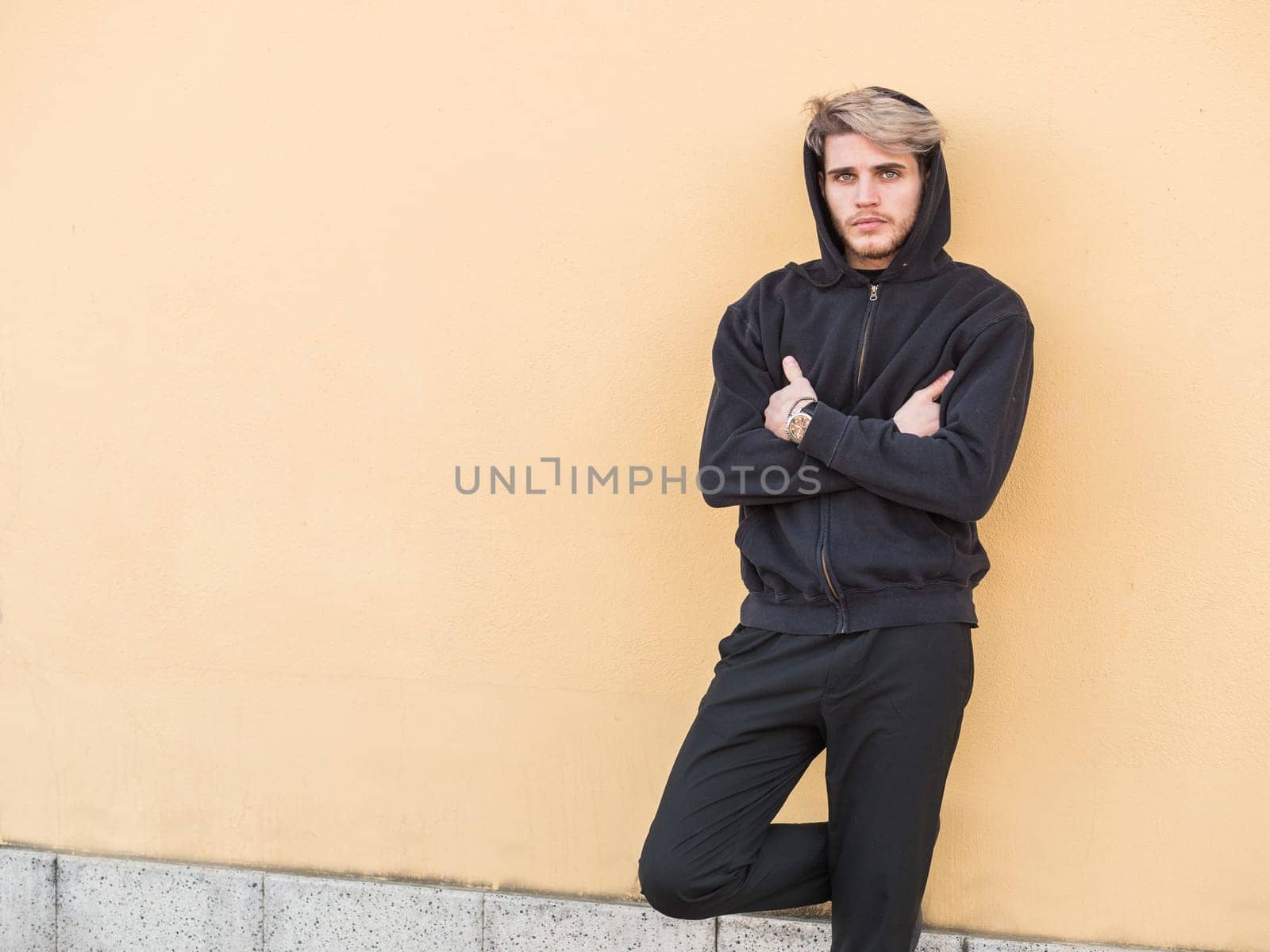 A man leaning against a wall with his arms crossed. Photo of a man with a confident pose leaning against a wall