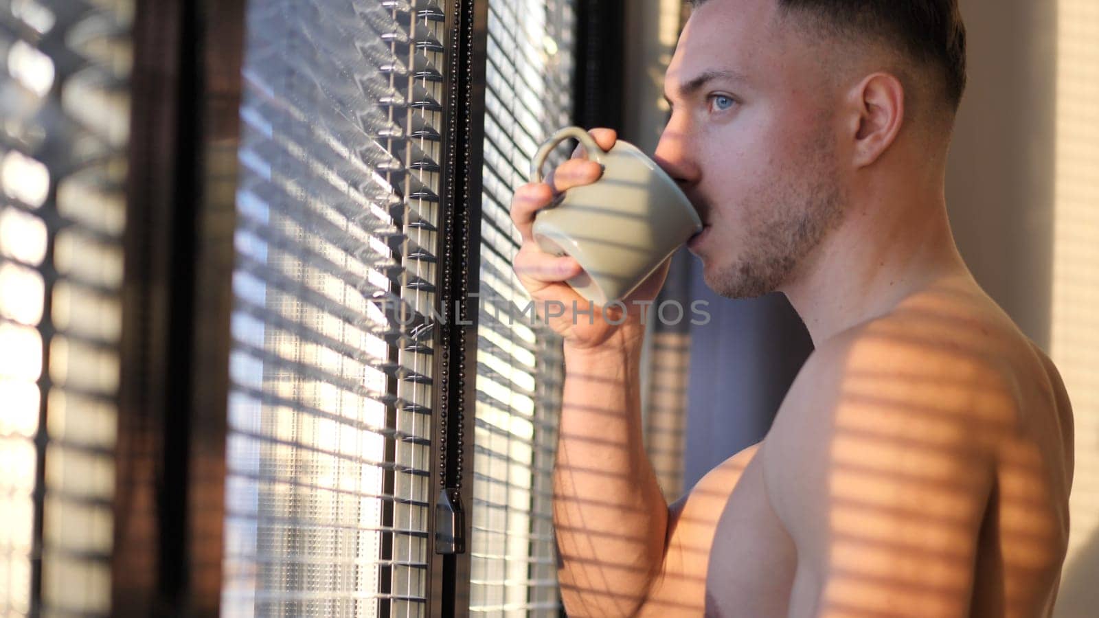 A shirtless man drinking from a mug. Photo of a man enjoying a refreshing drink