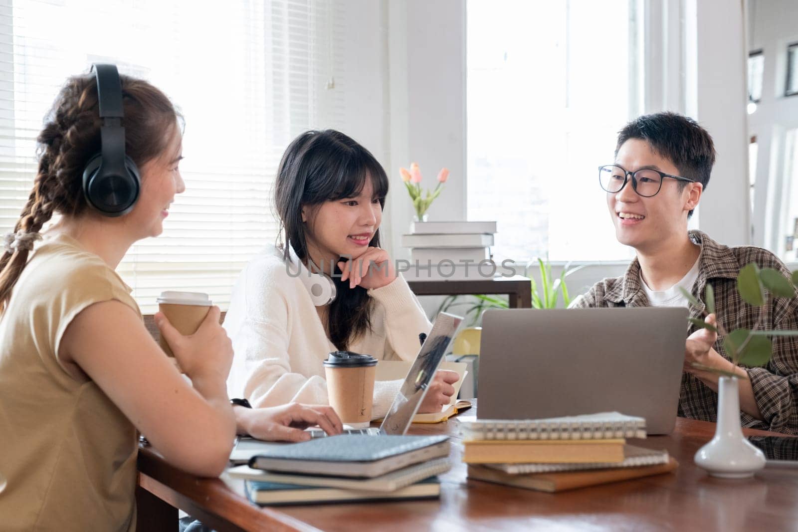 A group of cheerful Asian college students are enjoying talking and discussing their group project while sitting in a coffee shop together..