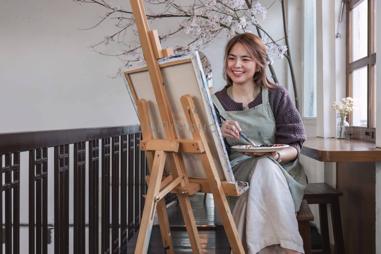 Young female artist works on abstract acrylic painting on canvas in art painting studio. by wichayada