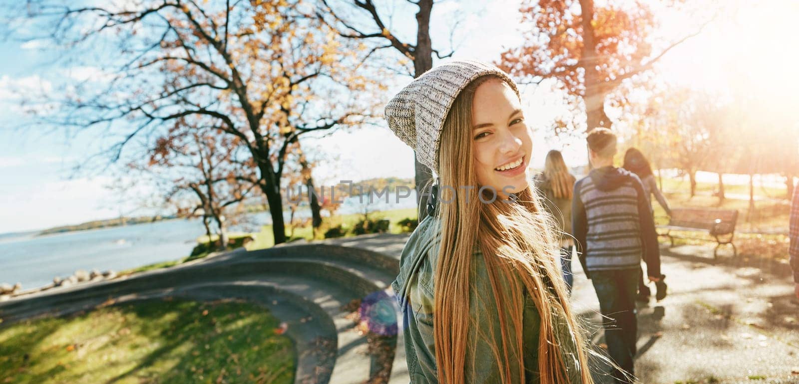Teen girl in nature with friends, walk in park with autumn and sunshine, wellness with happiness in portrait. Youth outdoor, enjoy fresh air and bonding with smile, flare with adventure or travel by YuriArcurs