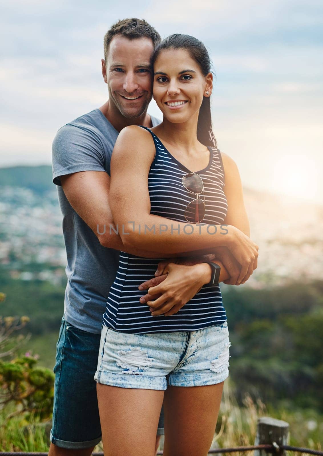 Portrait, hug and couple with happiness, outdoor and lens flare with holiday, romance and vacation. Face, man and woman with bonding, adventure and health with fun, outside and wellness with love by YuriArcurs