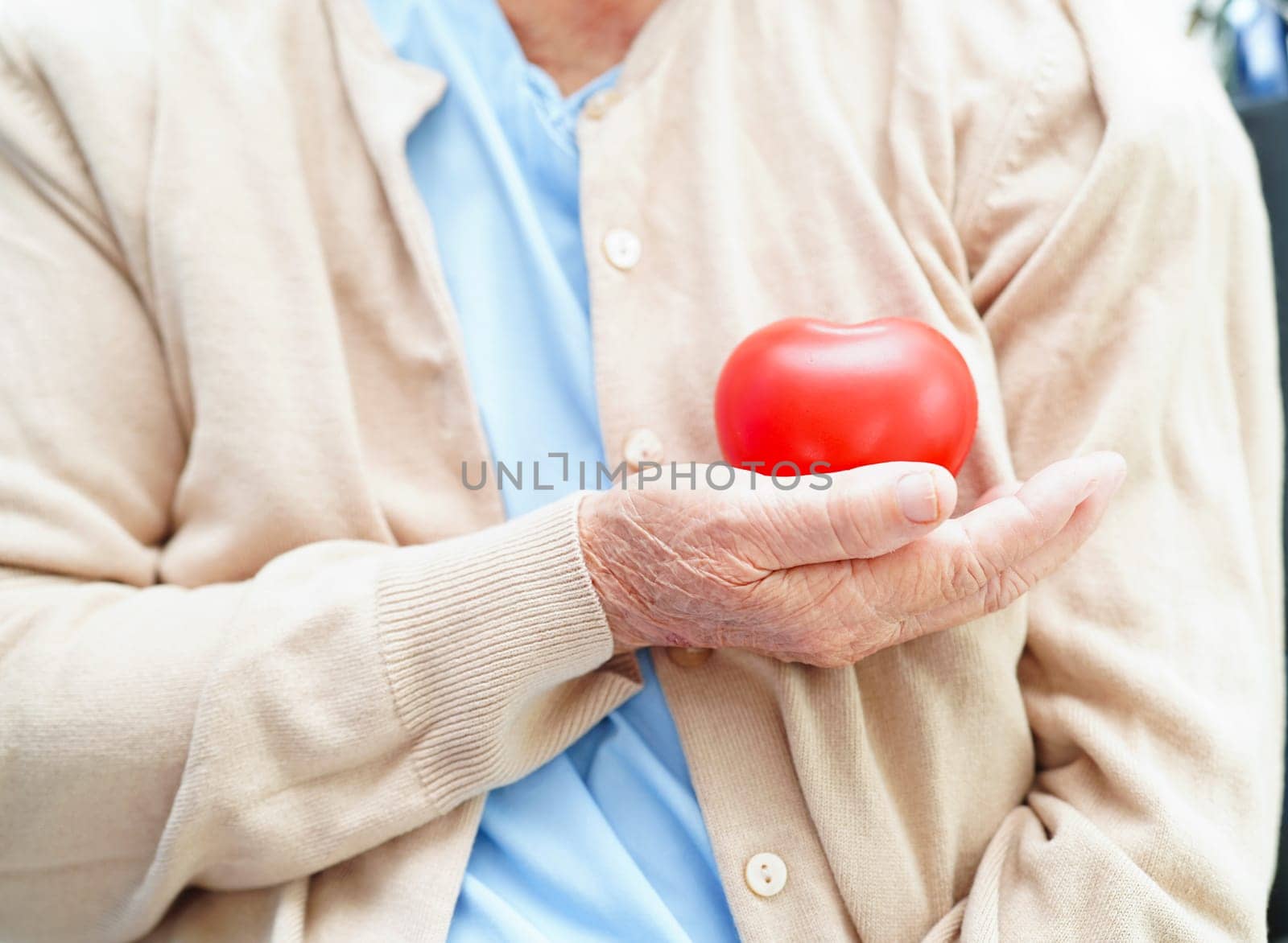 Asian elder senior woman patient holding red heart in hospital.