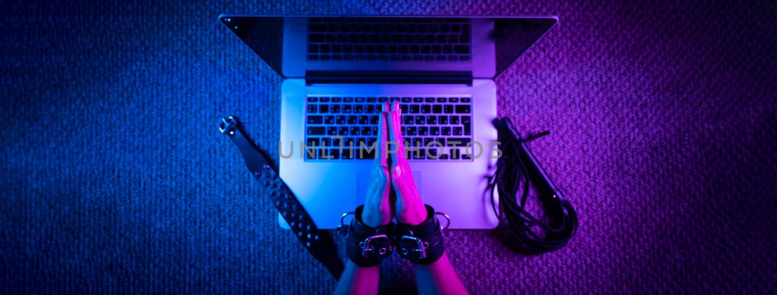 the female sexy hands in bdsm handcuffs with laptop in neon light on dark background