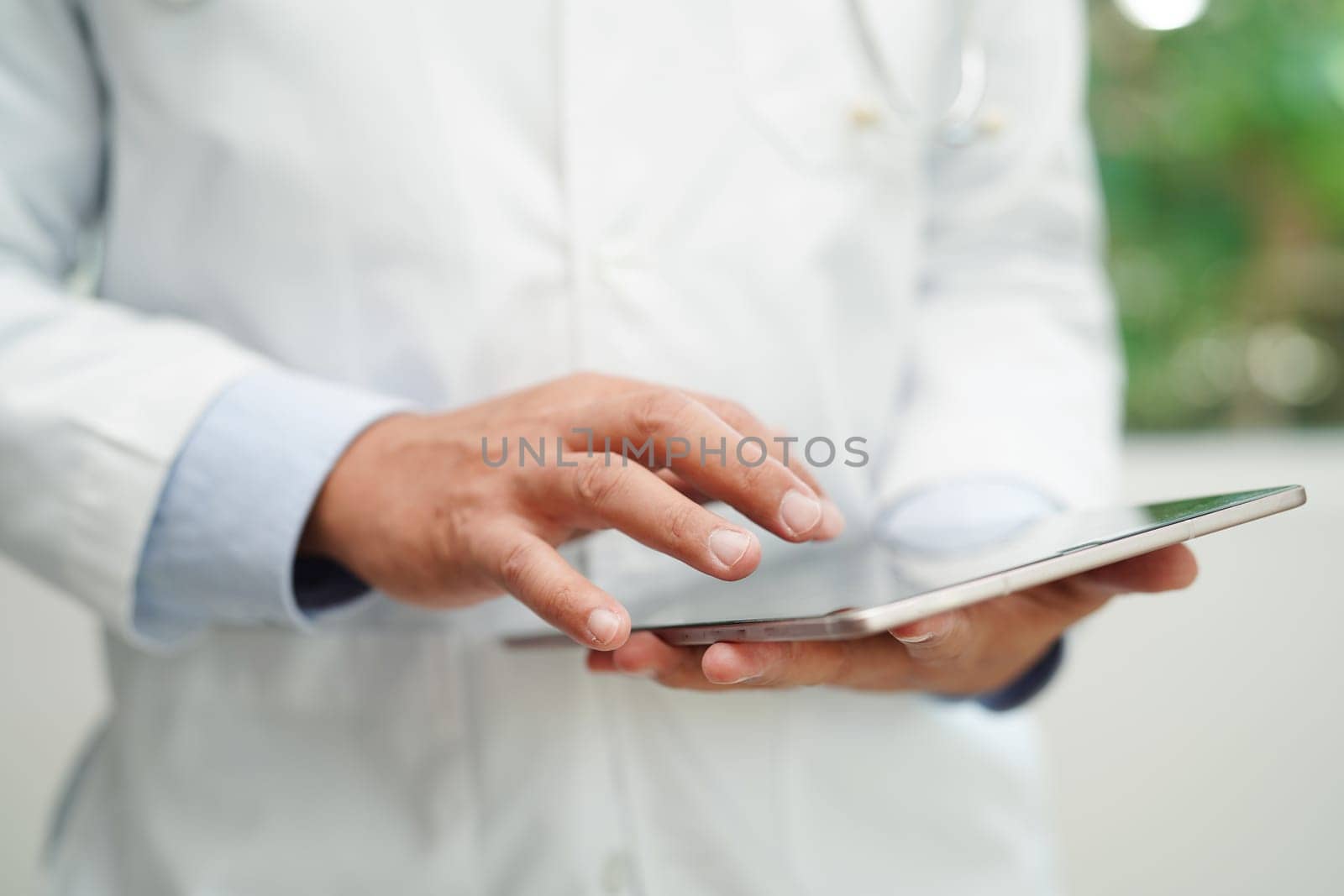 Asian man doctor using tablet computer to reading patient report, check up and search for solve treatment health medical online in hospital.