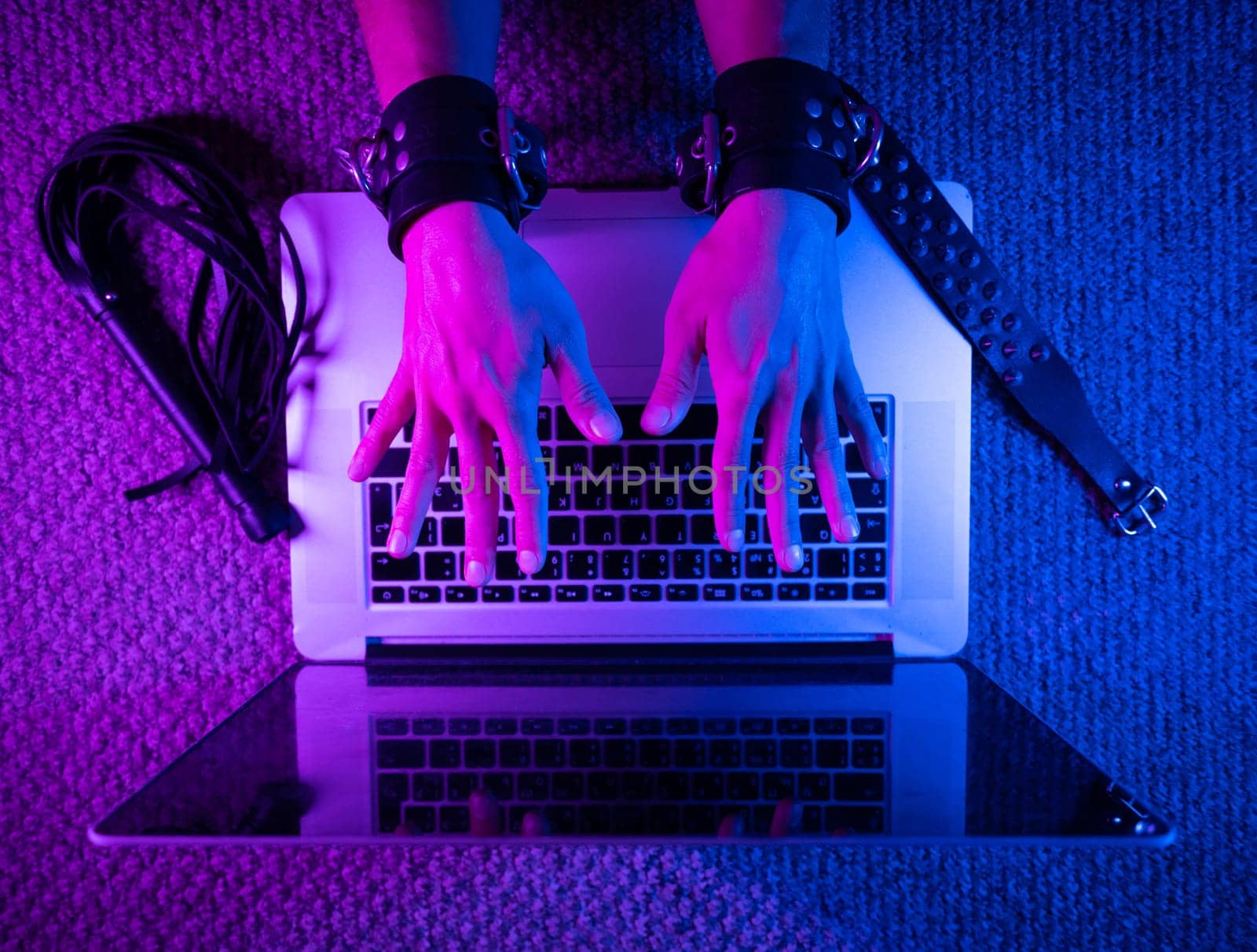 female sexy hands in bdsm handcuffs with laptop in neon light on dark background by Rotozey