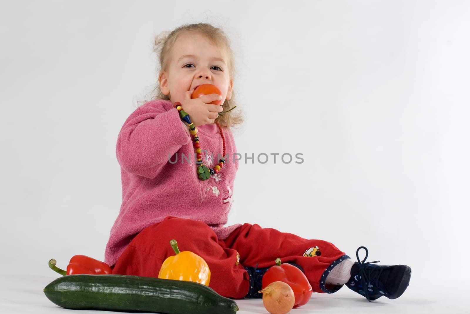 Child sitting among vegetables and biting into a tomato