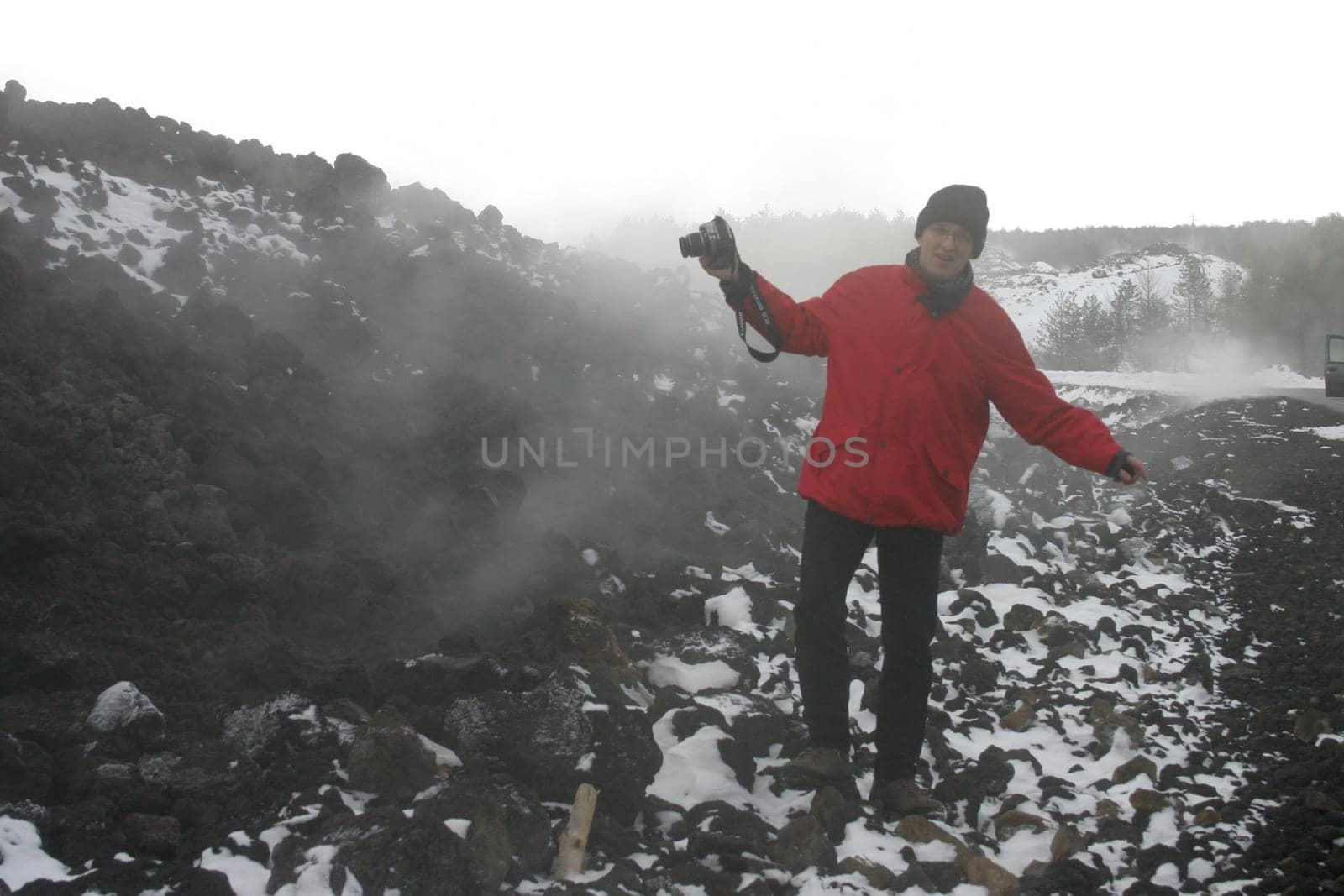 Man in red jacket with camera on the still steaming lava field of Mount Etna near Zafferano (Sicily)