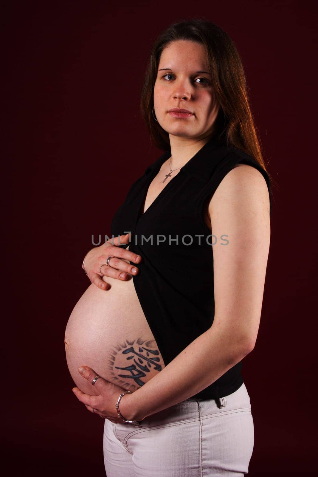The photo shows a standing,pregnant woman with a tattoo