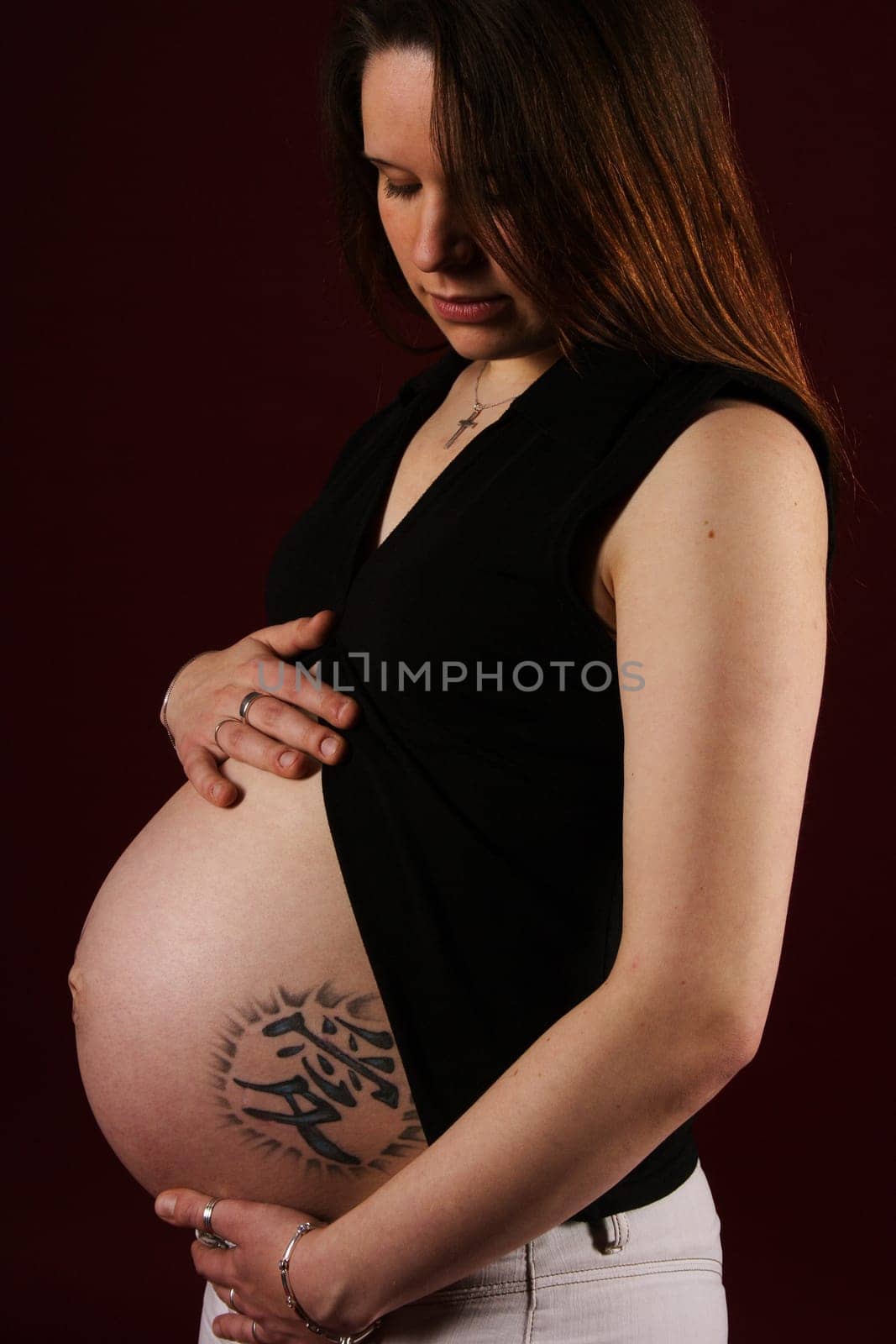 A pregnant woman stands,sensually looking at her stomach