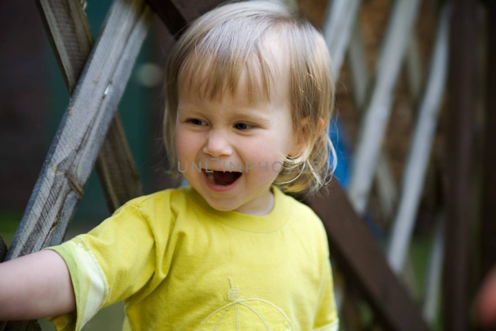 A little girl stands in front of a fence and has her mouth wide open..... As if she's calling someone or laughing out loud