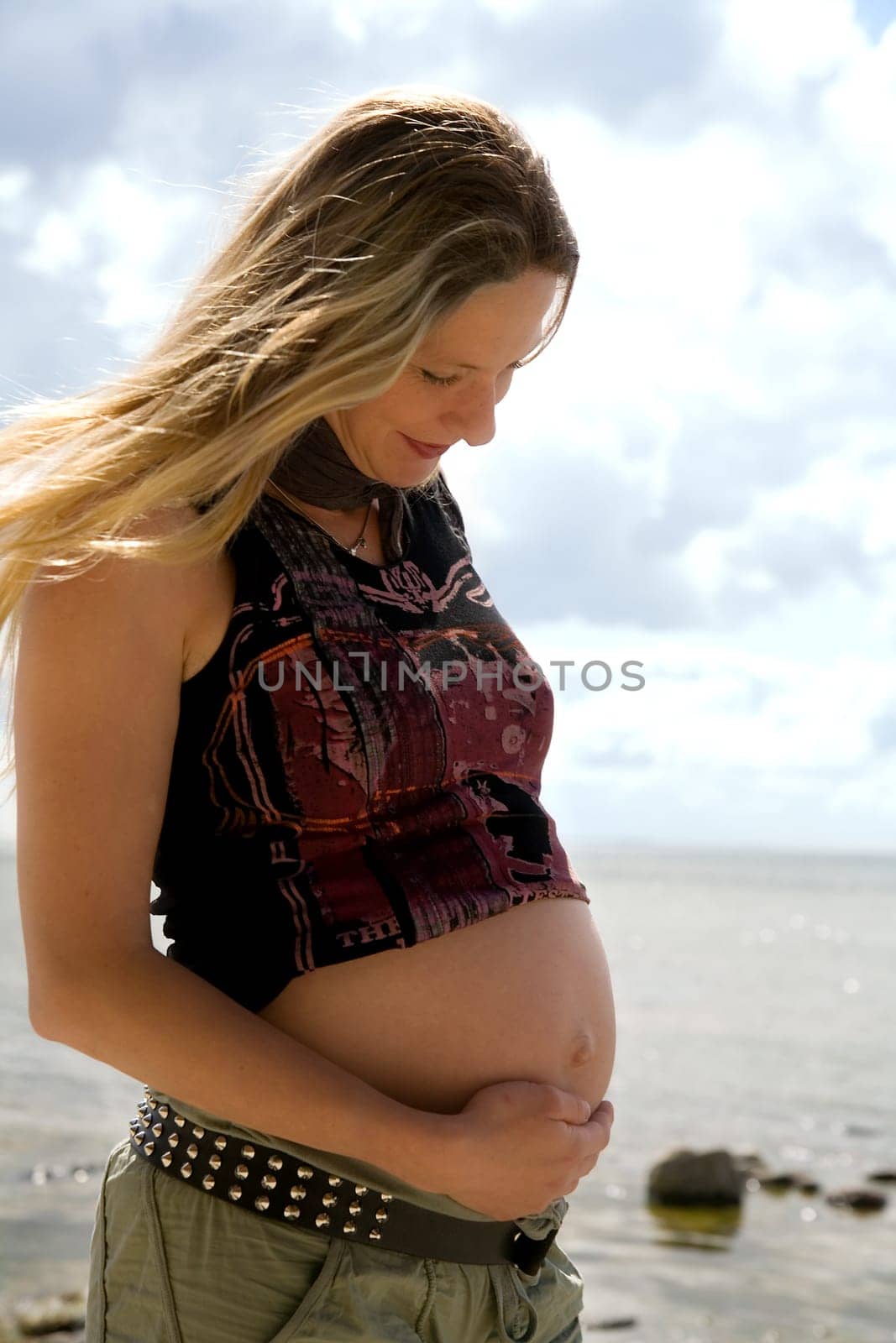 A young pregnant woman stands on the beach and feels the movements of the unborn child