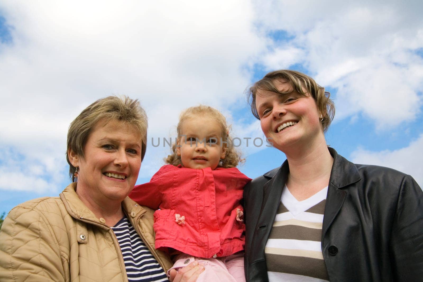 Mother,daughter and grandchild together in front of a blue,slightly cloudy sky