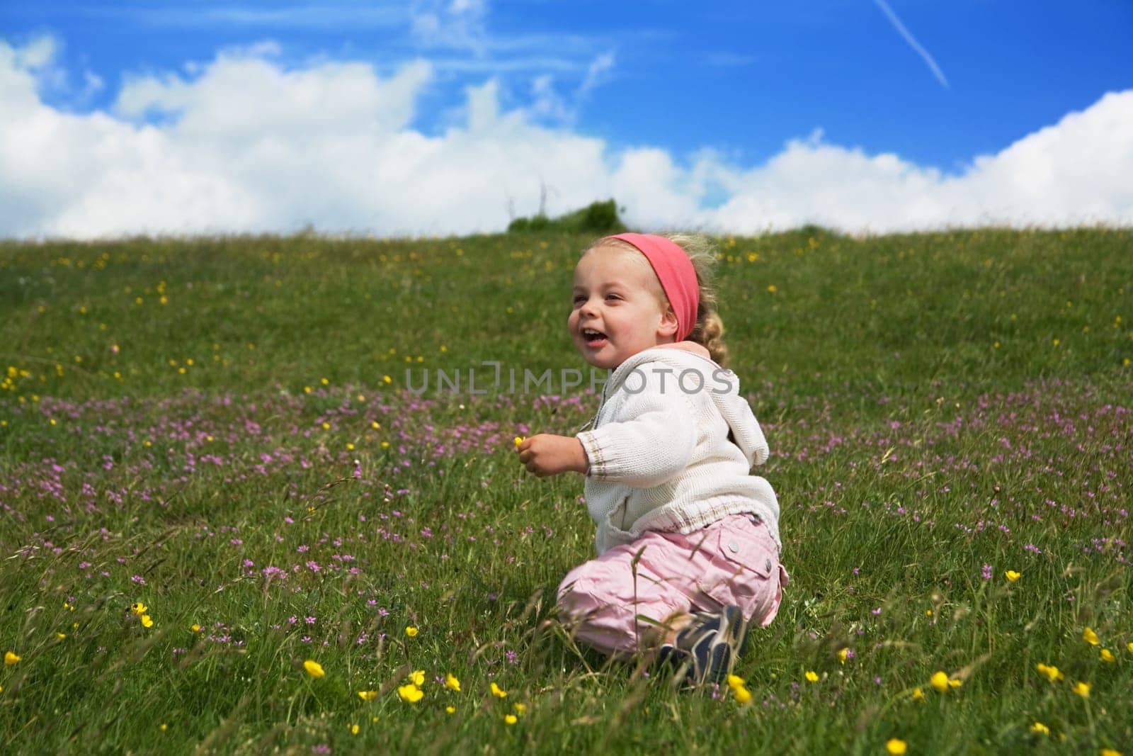 A little girl plays on a summer meadow in front of a blue,slightly cloudy sky.