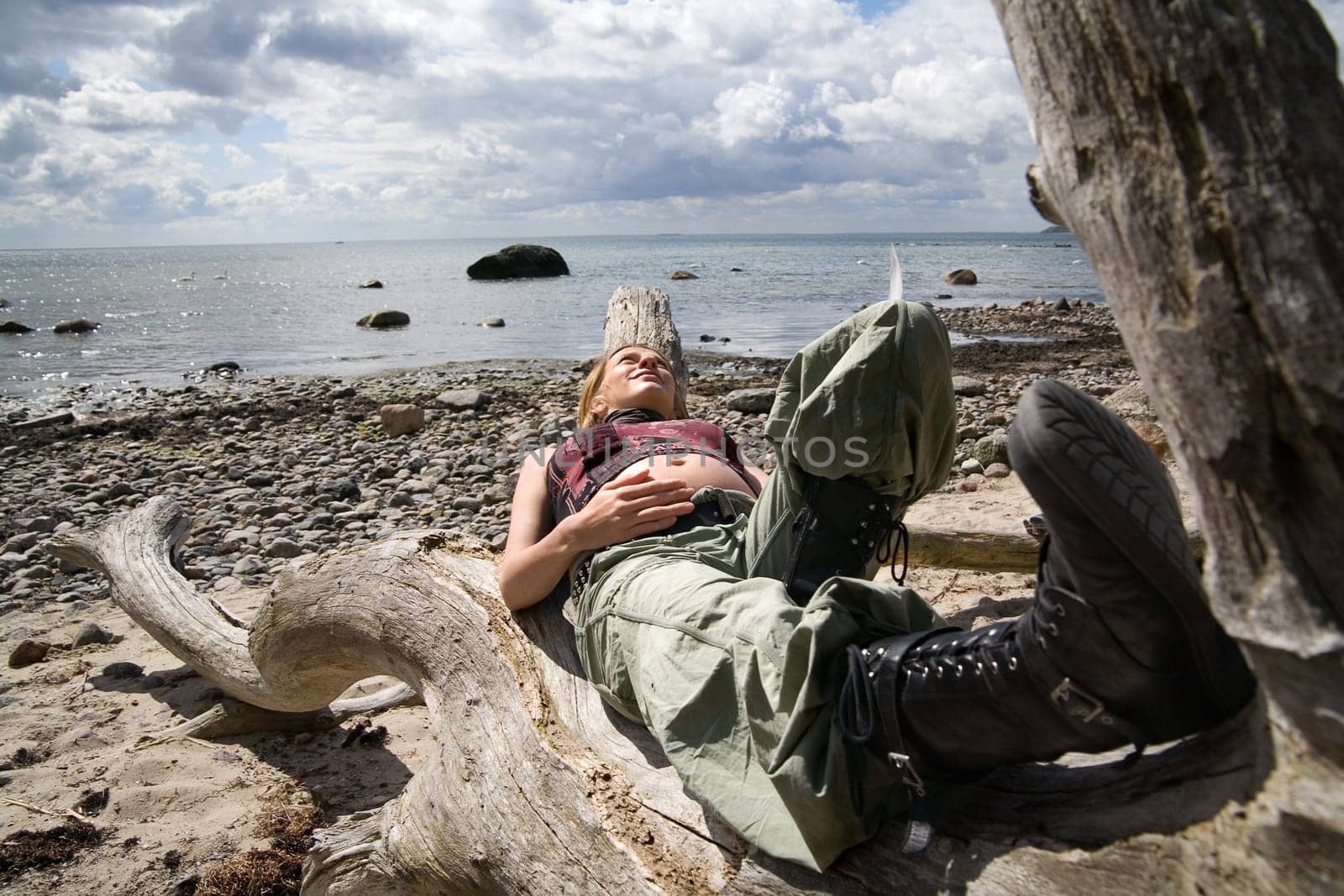 A young pregnant woman lies on a dead tree on the beach in the background the sea