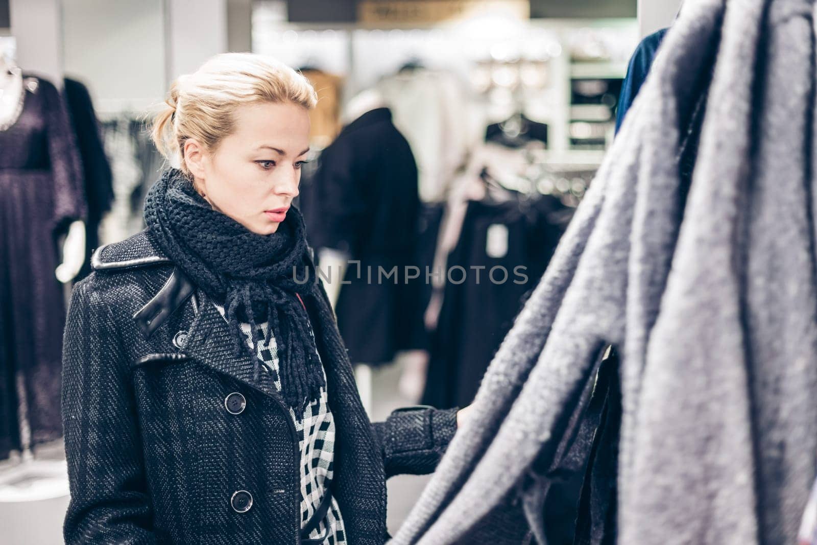 Woman shopping clothes. Shopper looking at clothing indoors in store. Beautiful blonde caucasian female model.
