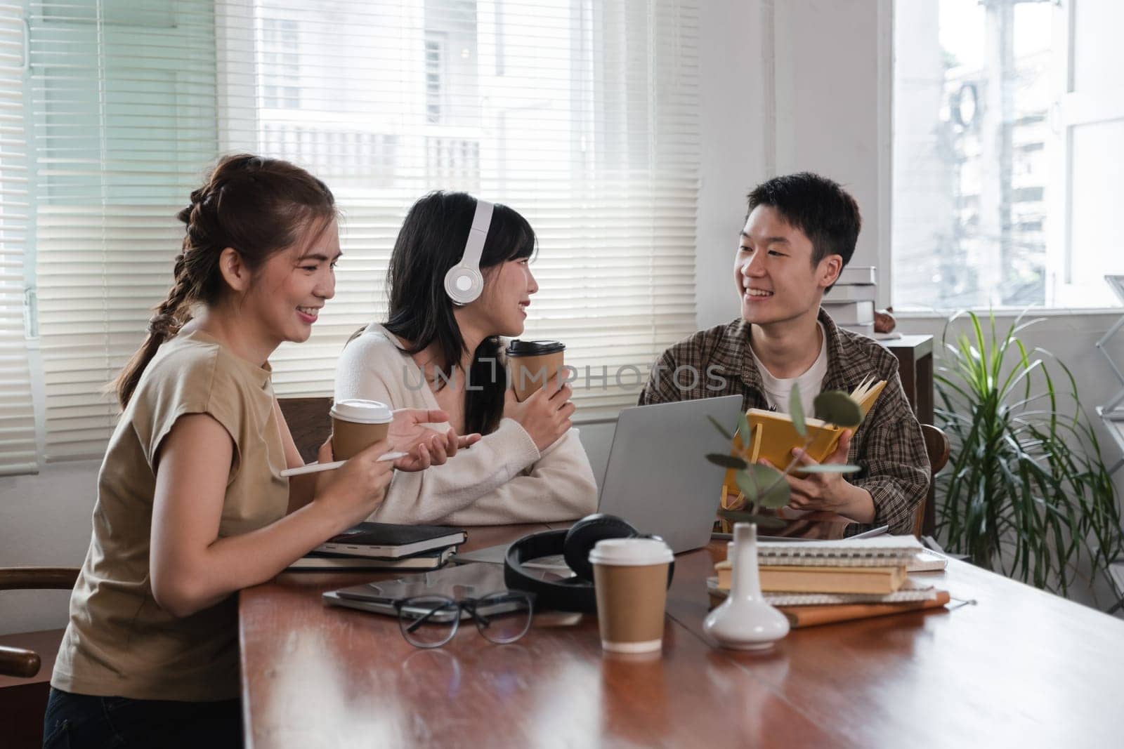 A group of cheerful Asian college students are enjoying talking and discussing their group project while sitting in a coffee shop together. by wichayada