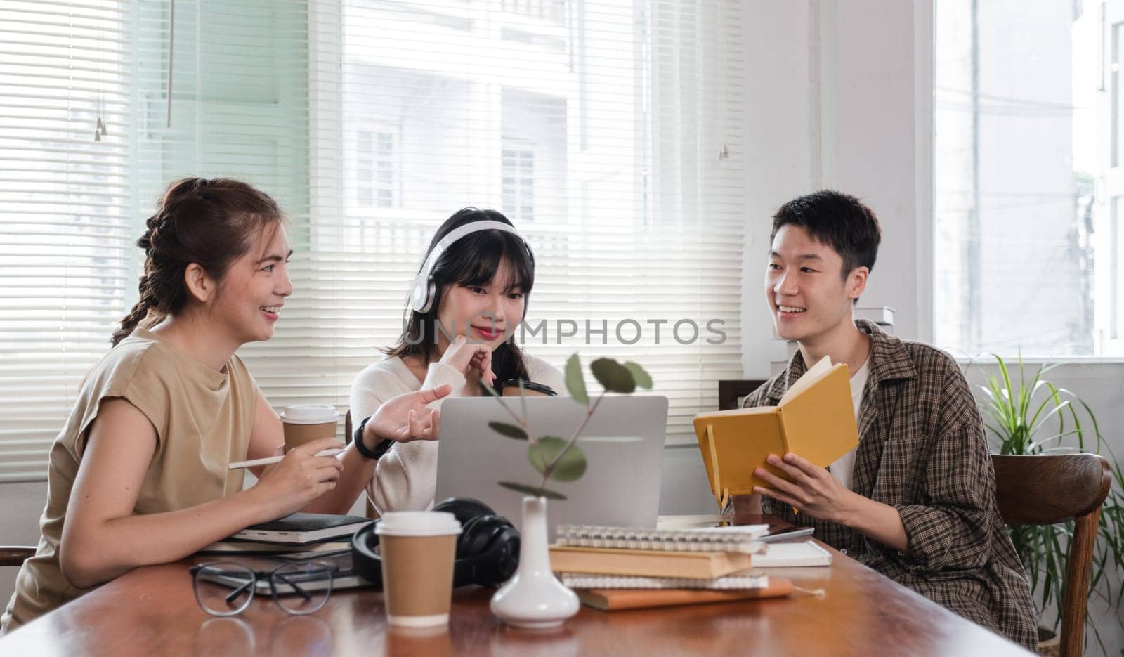 A group of cheerful Asian college students are enjoying talking and discussing their group project while sitting in a coffee shop together. by wichayada