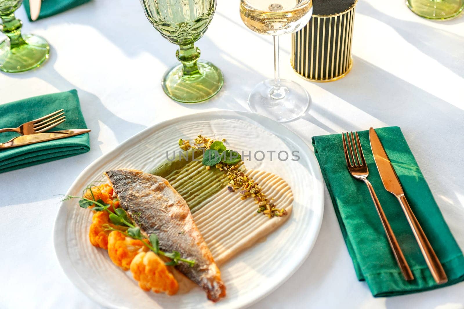 Grilled sea bass fillet with with cauliflower, sauce and pistachio. Food lies on a light ceramic plate on a table in a restaurant.